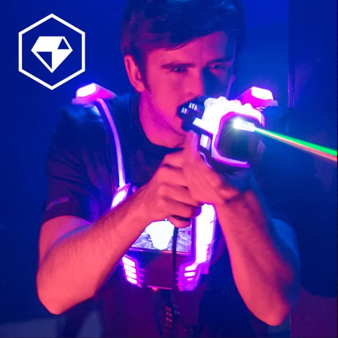 Erwachsener beim Lasertag mit leuchtender Weste und Phaser, grüner Laserstrahl in einer dunklen Indoor-Lasertag-Arena.