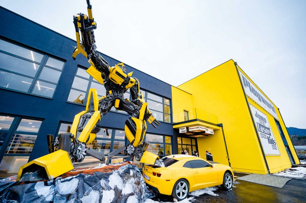 Außenansicht des Laserdance.at-Gebäudes im Wiener Prater mit gelber Fassade, großem Roboter-Modell und gelbem Sportwagen.