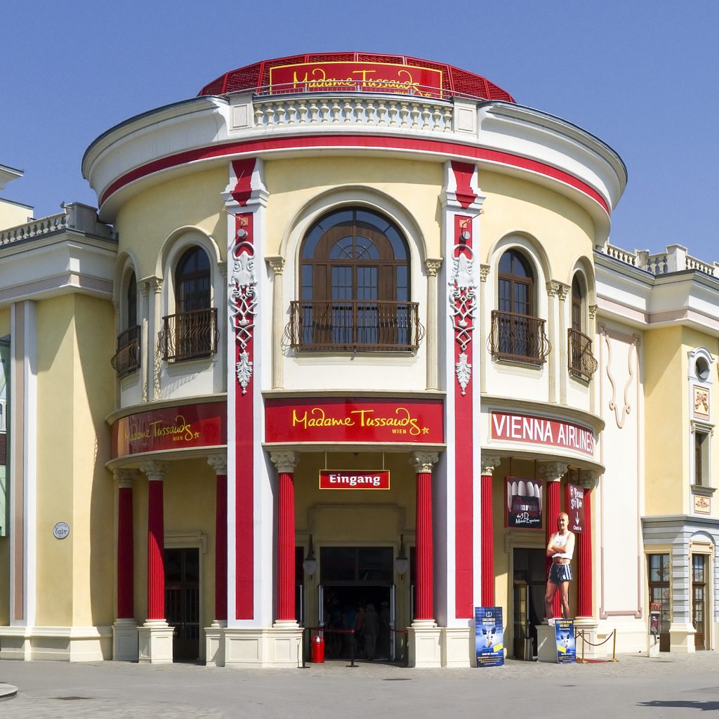 Historisches Gebäude von Madame Tussauds Wien mit gelber Fassade, roten Säulen und zentralem Eingang.