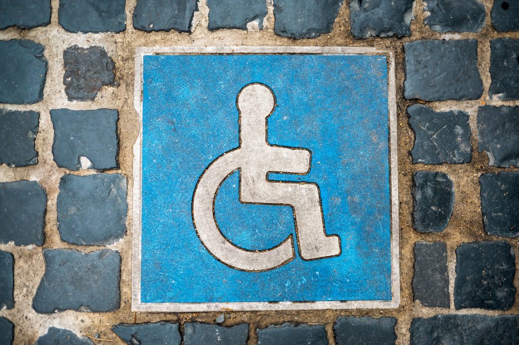 Blaues Rollstuhlsymbol als Bodenmarkierung für einen barrierefreien Parkplatz auf dunklem Kopfsteinpflaster.