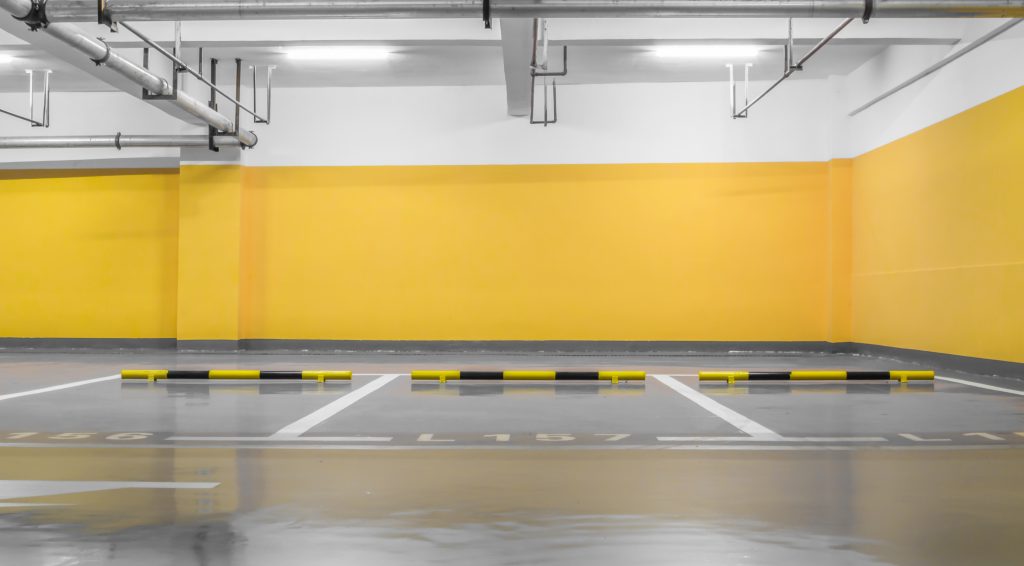 Leere Tiefgarage mit gelben Wänden, markierten Stellplätzen und schwarz-gelben Radstoppern.