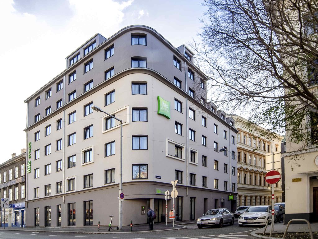 Mehrstöckiges Stadthotel mit heller Fassade und abgerundeter Gebäudeecke an einer innerstädtischen Kreuzung.