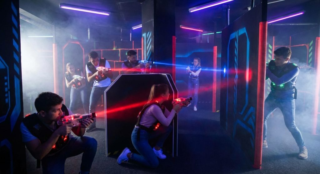 Mehrere Personen spielen Lasertag mit leuchtenden Westen und Markierern zwischen Deckungen in einer nebeligen Neon-Arena.