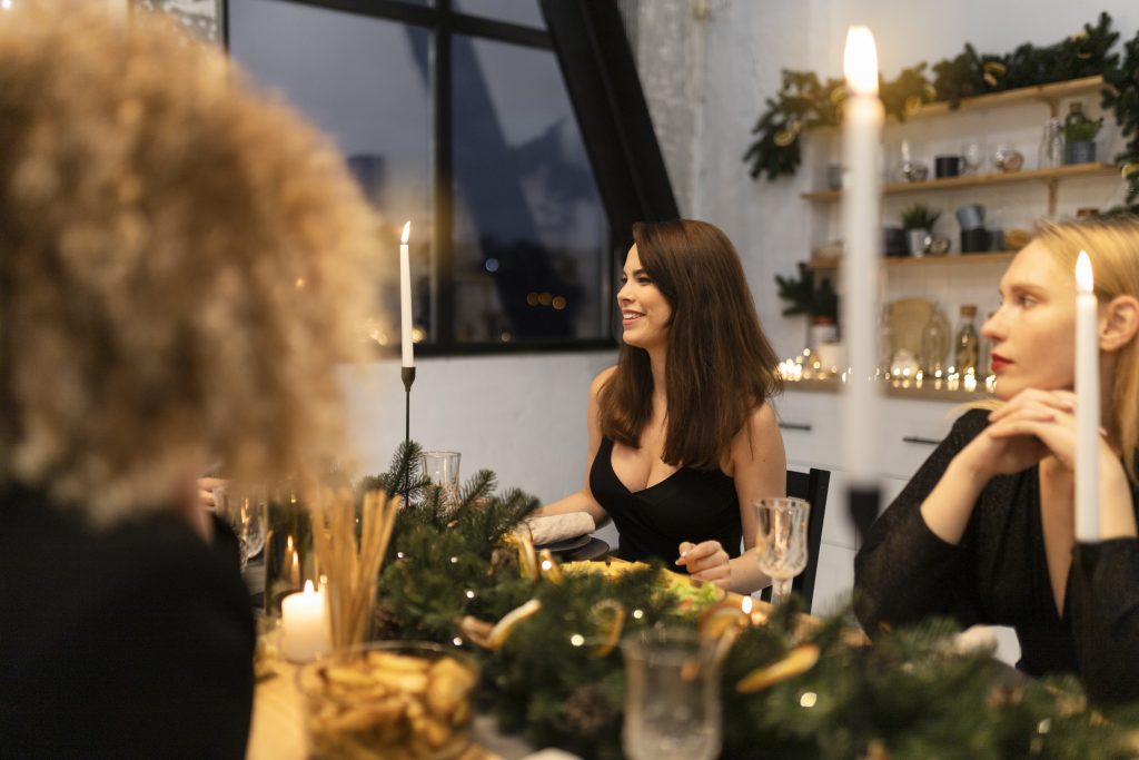 Mehrere Frauen sitzen bei Kerzenlicht an einer festlich mit Tannengrün und goldenen Elementen dekorierten Tafel.