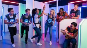 Gruppe junger Menschen mit leuchtenden Lasertag-Westen feiert mit High Five in einer neonbeleuchteten Arena