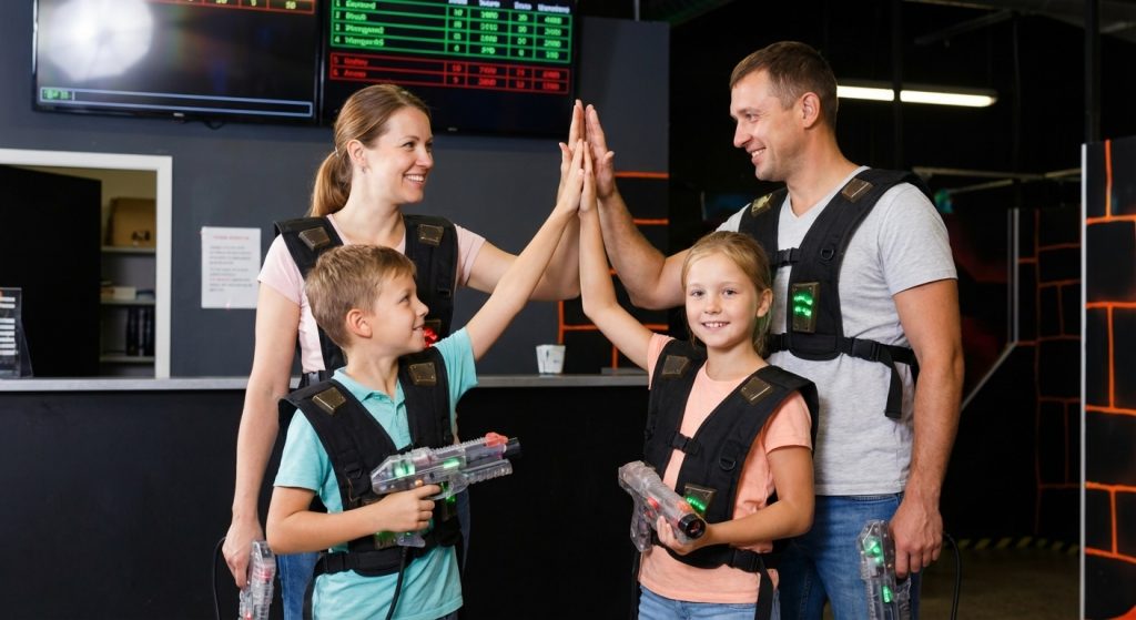 Familie mit zwei Kindern gibt sich nach dem Lasertag-Spiel ein High-Five und trägt leuchtende Westen mit Markierern.