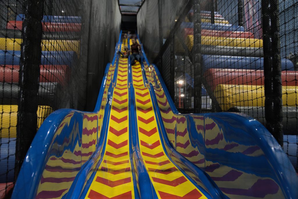 Mehrbahnige Indoor-Rutsche mit gelb-roten Bahnen und Kindern in einer Freizeithalle