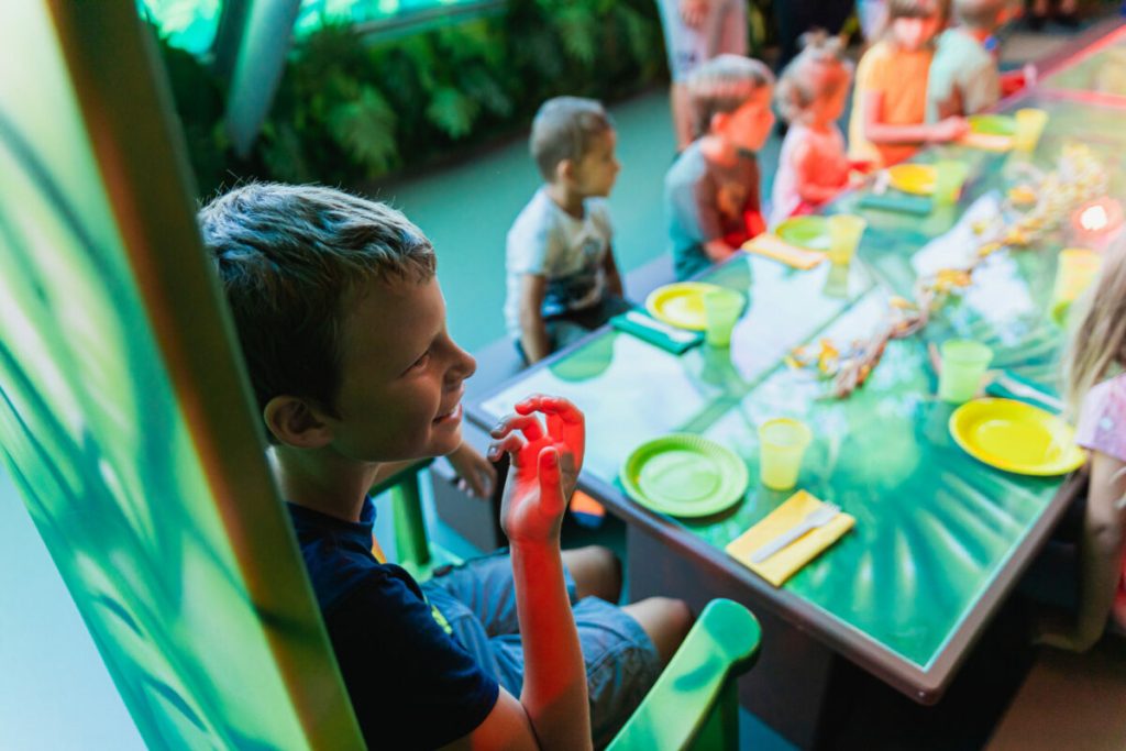 Kinder sitzen an einem gedeckten Geburtstagstisch mit buntem Licht in einer Indoor-Spielhalle