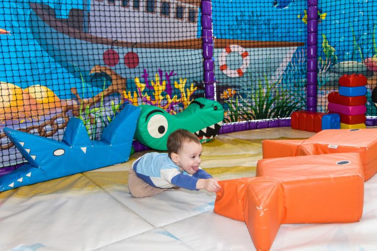 Kleinkind spielt auf weichen Kletterelementen in einer bunten Indoor-Spielhalle mit Tiermotiven
