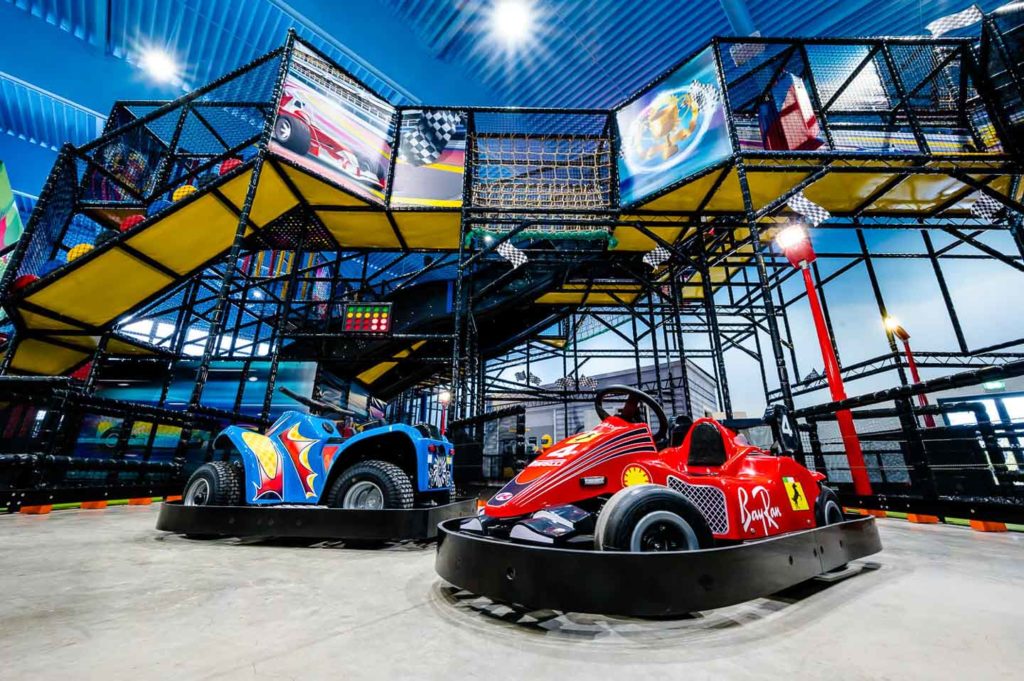 Indoor-Kartbahn mit bunten Go-Karts und mehrstöckigem Klettergerüst in einer Freizeithalle