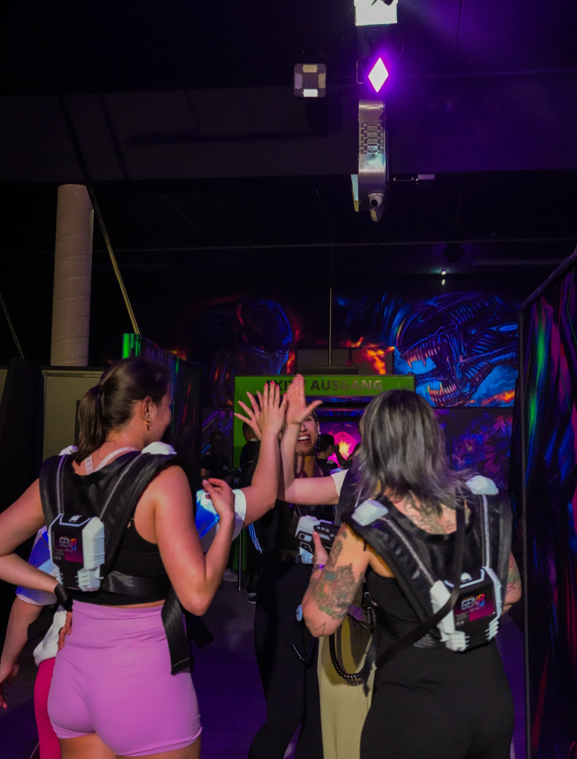 Gruppe von Lasertag-Spielern mit Westen und Phasern beim High-Five nach dem Spiel in einer neonbeleuchteten Indoor-Lasertag-Arena.