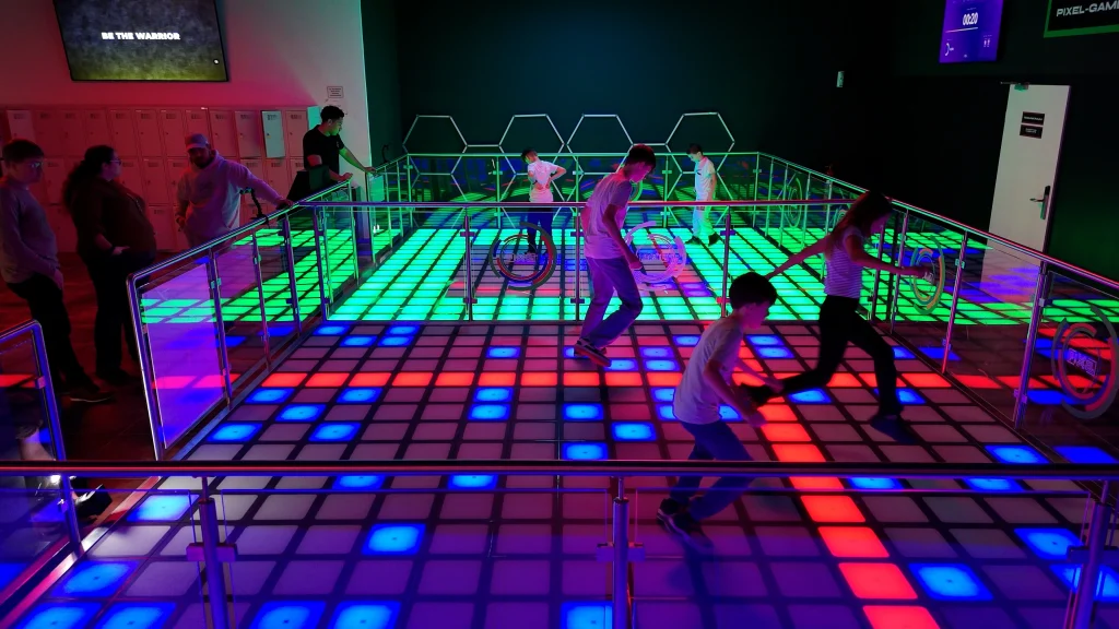 Kinder und Erwachsene auf interaktiver LED-Tanzfläche mit farbigen Leuchtfeldern in moderner Indoor-Freizeitanlage.