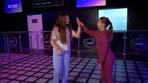 Zwei Kinder geben sich ein High-Five auf einer beleuchteten Tanzfläche in einer modernen Indoor-Freizeitanlage.